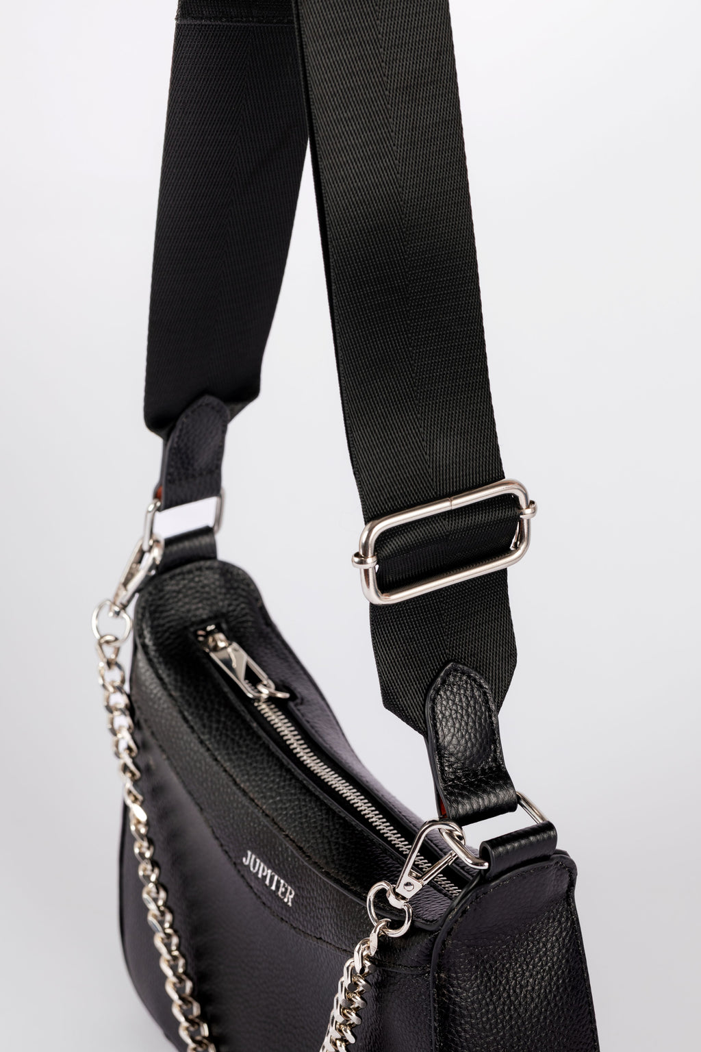 A close-up of a black leather shoulder bag with a wide black webbing strap, silver-tone metal hardware, and a silver chain detail. The brand name 'JUPITER' is visible on the side of the bag. The travel bag includes safety features to keep valuables safe when on holiday or travelling